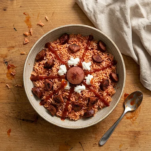 Tomato Lava Bowl mit Chorizo-Stücken, Ketchup-Lavastrahlen und Sauerrahm-Tupfen rund um den Reis angerichtet