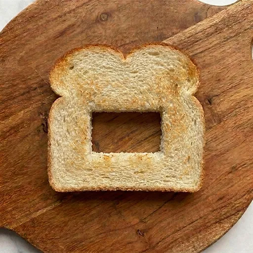 Plain toasted bread slice with a rectangular window cut out of the center, the base shape for Halloween Toasti